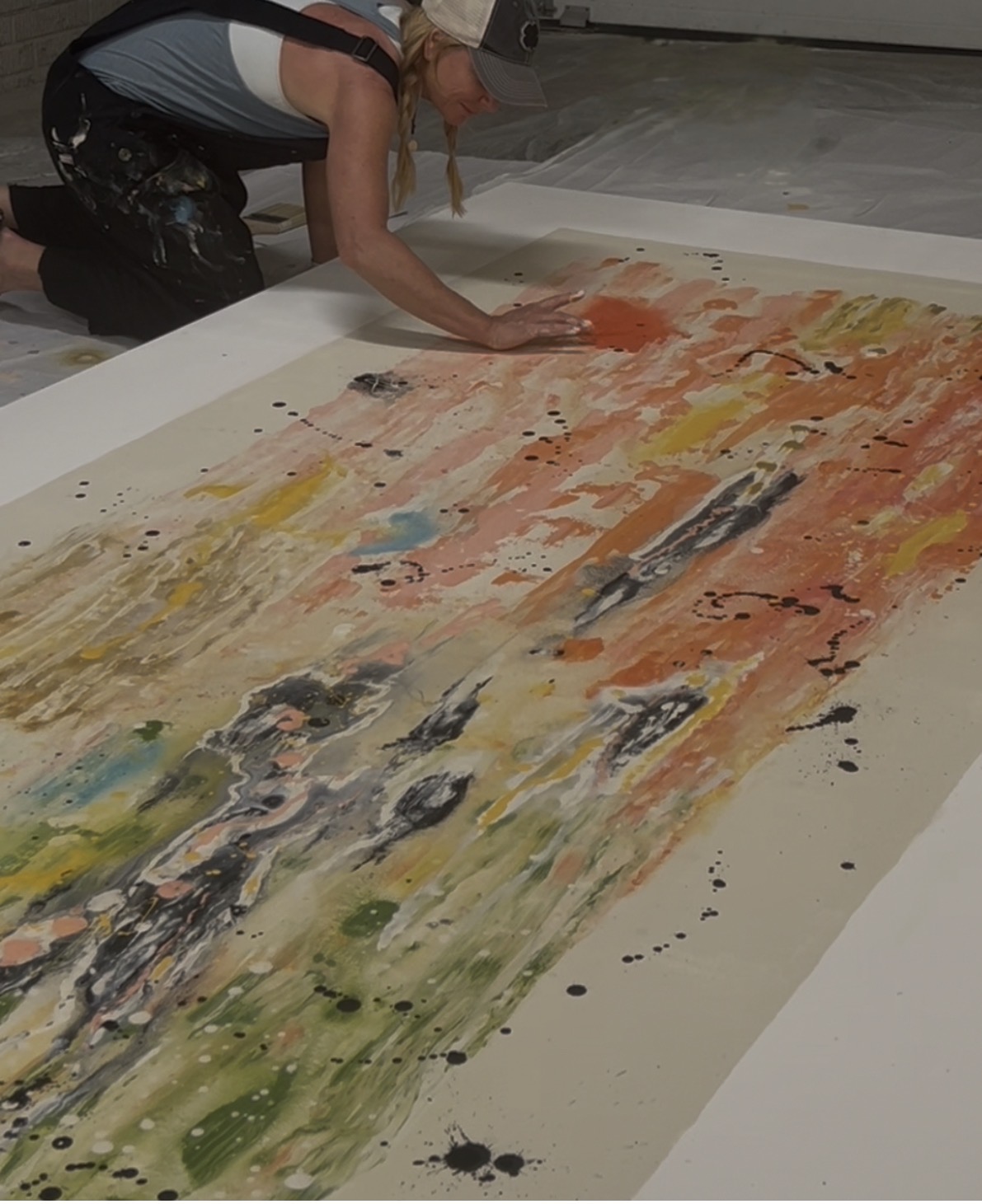 Artist working on a large-scale abstract painting laid out on the studio floor
